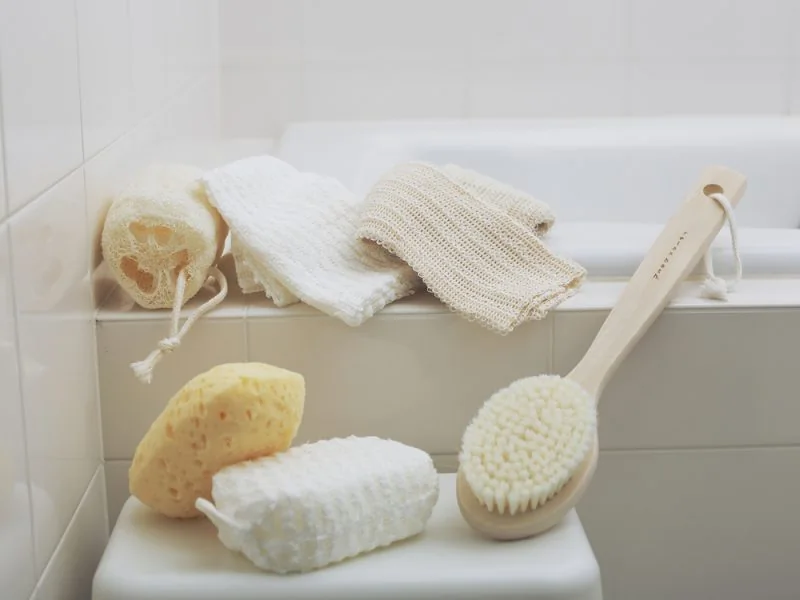 Bath sponges, a body brush and a towel on the edge of a bathtub