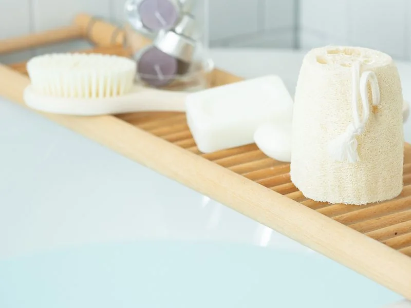 A bath tray with a body brush, soap and a loofah