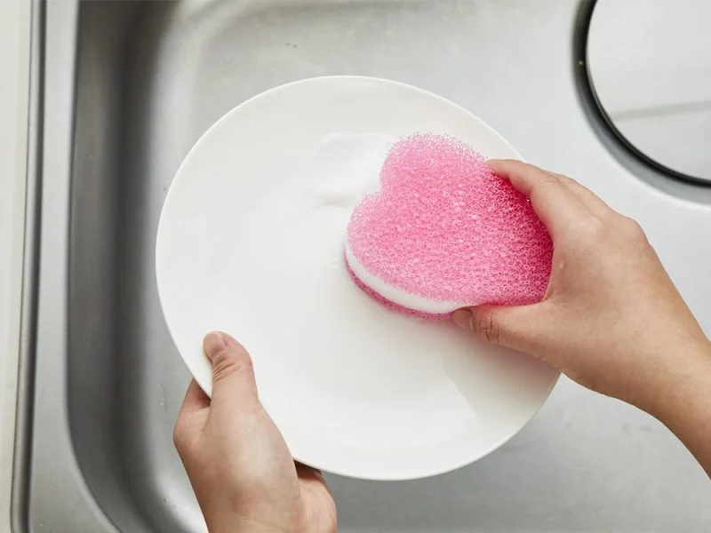 Washing a plate with a pink kitchen sponge