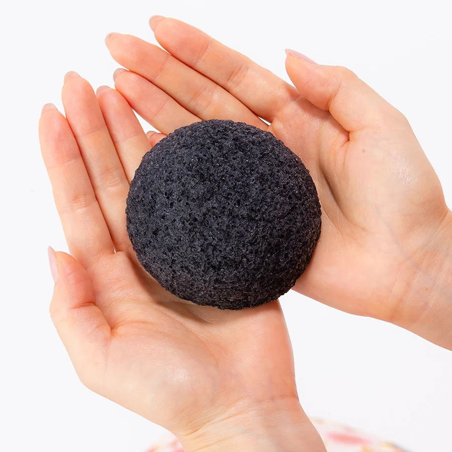 Charcoal konjac face sponge held in two hands