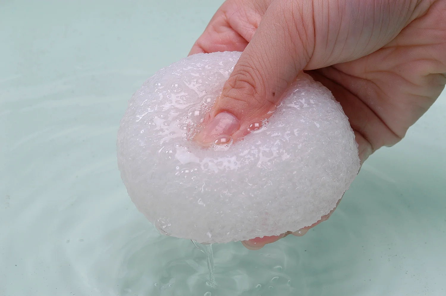 A hand pressing a wet konjac sponge in a basin of water